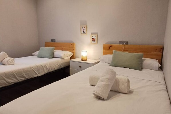 A hotel room with two beds, each with a wooden headboard, white linens, and a small bedside table with a lamp.
