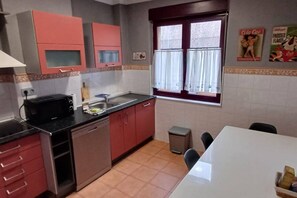 A compact kitchen with red cabinets, a microwave, and a sink. - 175A La Arena 3-Bedroom Apartment by R2R Consulting (Gijón)