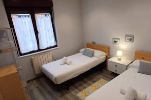 Ein kleines, ordentliches Schlafzimmer mit einem Einzelbett, einem Nachttisch mit Lampe, einem Fenster mit Vorhängen und einer Heizung.