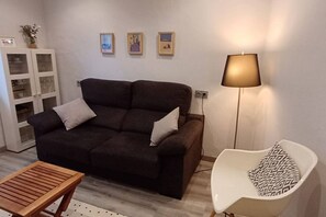 A living room with a dark brown sofa, a wooden coffee table, a white armchair, a floor lamp, and a cabinet with glass doors.