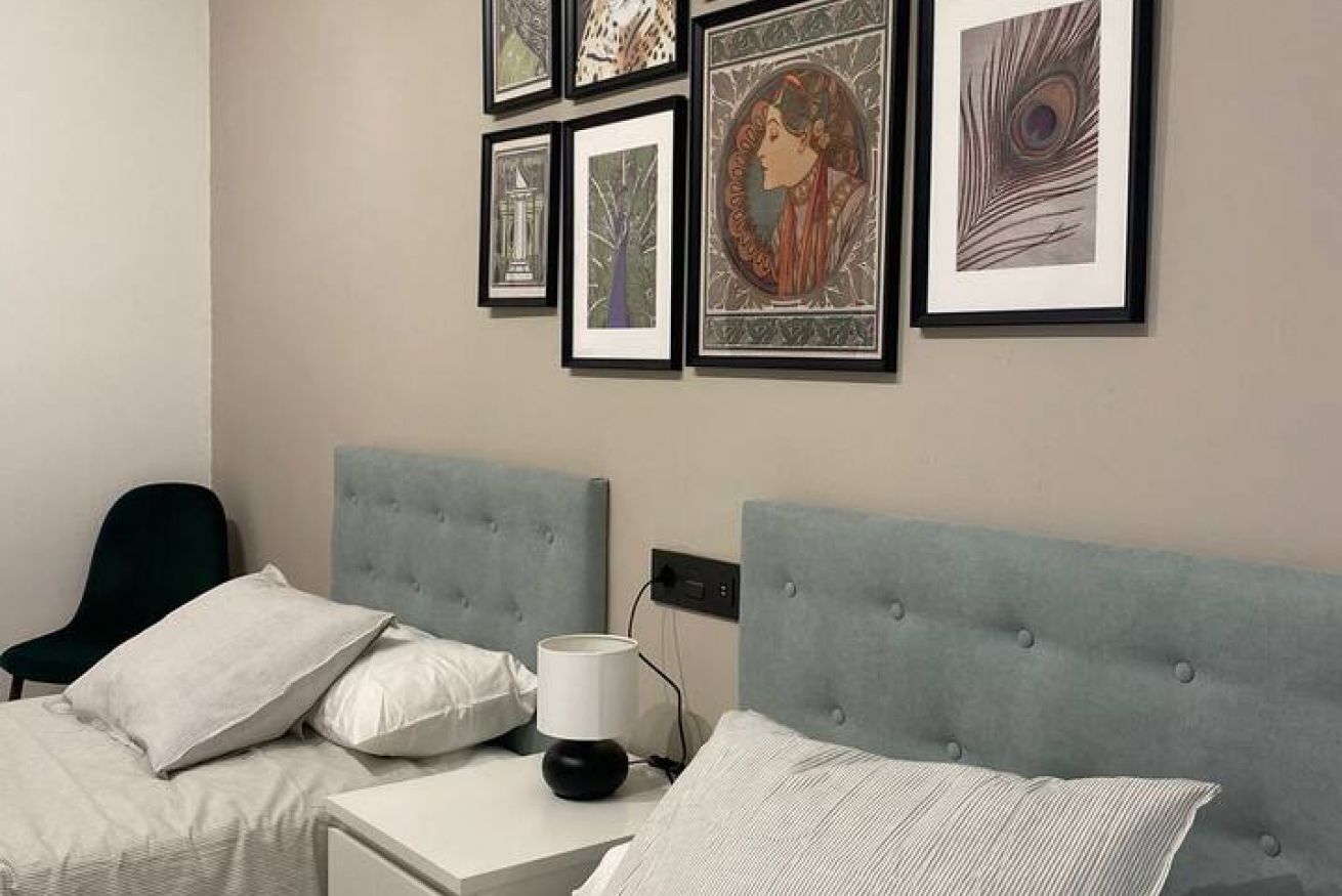 Een slaapkamer met een bed, nachtkastje, lamp en een lijst met kunst aan de muur.