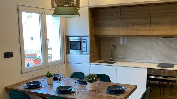 A modern kitchen with a built-in microwave, a sink, and a dining area with a wooden table set for two. - 176A Modern 3-Bedroom Apartment by R2R Consulting (Gijón)