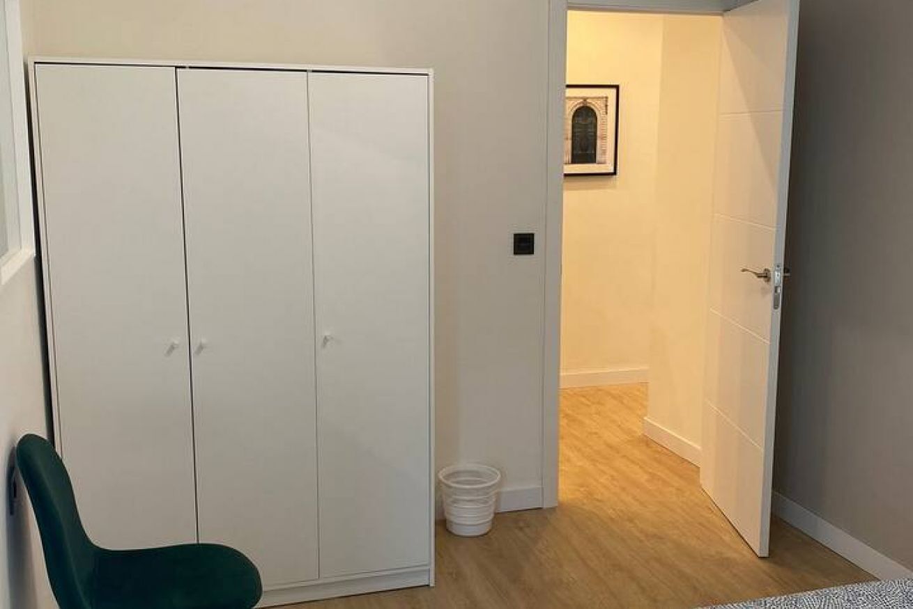 A room with a wardrobe, a chair, and a door leading to another room.
