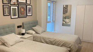 A bedroom with two beds, a nightstand, a lamp, a wardrobe, and framed artwork on the wall. - 176A Modern 3-Bedroom Apartment by R2R Consulting (Gijón)