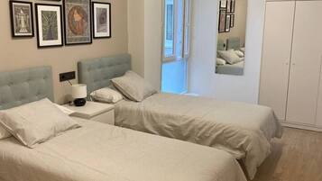 Un dormitorio con dos camas, una mesita de noche, una lámpara, un armario y cuadros en la pared.