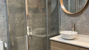 A modern bathroom with a glass shower enclosure, a white sink with a round basin, and a wooden vanity. - 176A Modern 3-Bedroom Apartment by R2R Consulting (Gijón)
