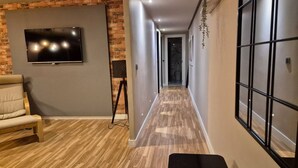 A hallway with a TV mounted on a brick wall, a bench, and a window with a grid pattern. - 184A Apartment in the La Arena neighborhood by R2R (Gijón)