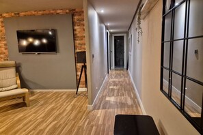 A hallway with a TV mounted on a brick wall, a bench, and a window with a grid pattern.