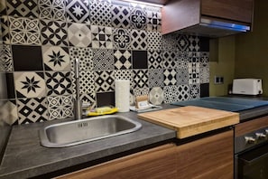 Una cocina con baldosas estampadas, un lavamanos de acero inoxidable, una tabla de cortar y un tostador.