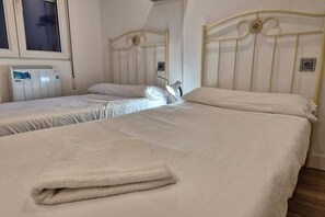 Una habitación con dos camas, un radiador, una ventana y una lámpara fijada a la pared.