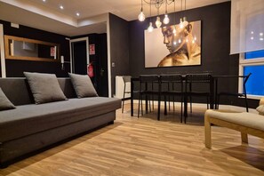 Een moderne woonkamer met een bank, eettafel, stoelen en een groot kunstwerk aan de muur.