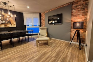 Una habitación con pared de ladrillo, un televisor sobre un escritorio, una silla y una mesa con sillas.