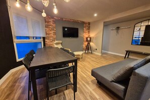 Una sala de estar moderna con una mesa de comedor, sofá y televisor montado en una pared de ladrillo.