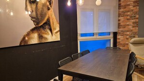 A dining area with a wooden table and chairs, a large artwork on the wall, and a kitchen with a brick wall and blue lighting. - 184A Apartment in the La Arena neighborhood by R2R (Gijón)