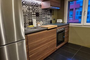 Una cocina con un refrigerador de acero inoxidable, armarios de madera, un microondas y una ventana con vistas a edificios.