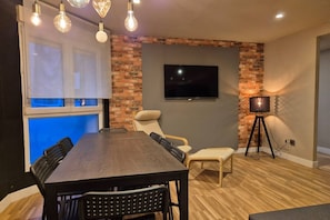 Un comedor moderno con pared de ladrillo decorativa, un televisor de pantalla plana y una lámpara con trípode.