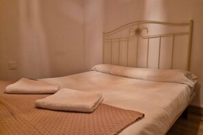 A single bed with a metal headboard, a beige blanket, and two folded towels.