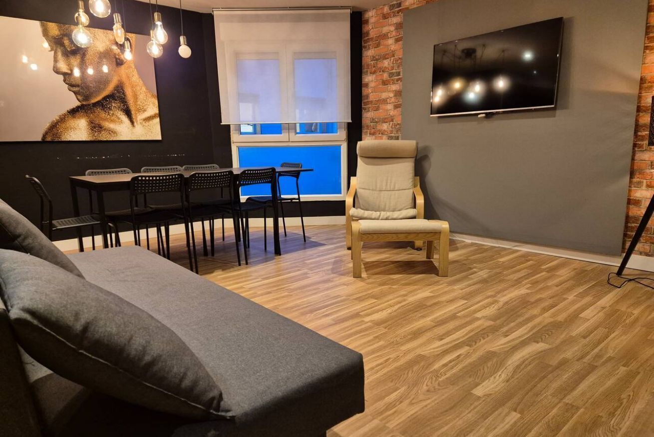 Ein modernes Wohnzimmer mit einer Couch, einem Essbereich mit Stühlen, einem an der Wand befestigten Fernseher und einer Wand aus Backsteinen.