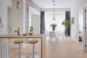 Eine moderne Küche mit einer zentralen Kochinsel, weißen Barhocker und einem Essbereich mit weißem Tisch und Stühlen.