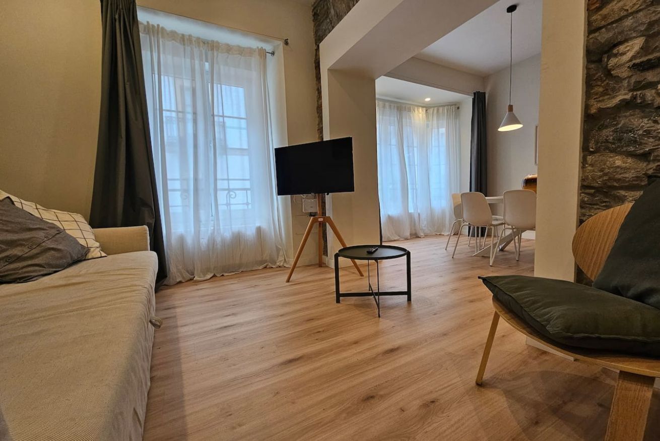 Un salon moderne avec un canapé, un téléviseur posé sur un pied, un coin repas avec des chaises et un mur d’accent en pierre.