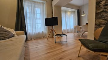 Un salon moderne avec un canapé, un téléviseur posé sur un pied, un coin repas avec des chaises et un mur d’accent en pierre.