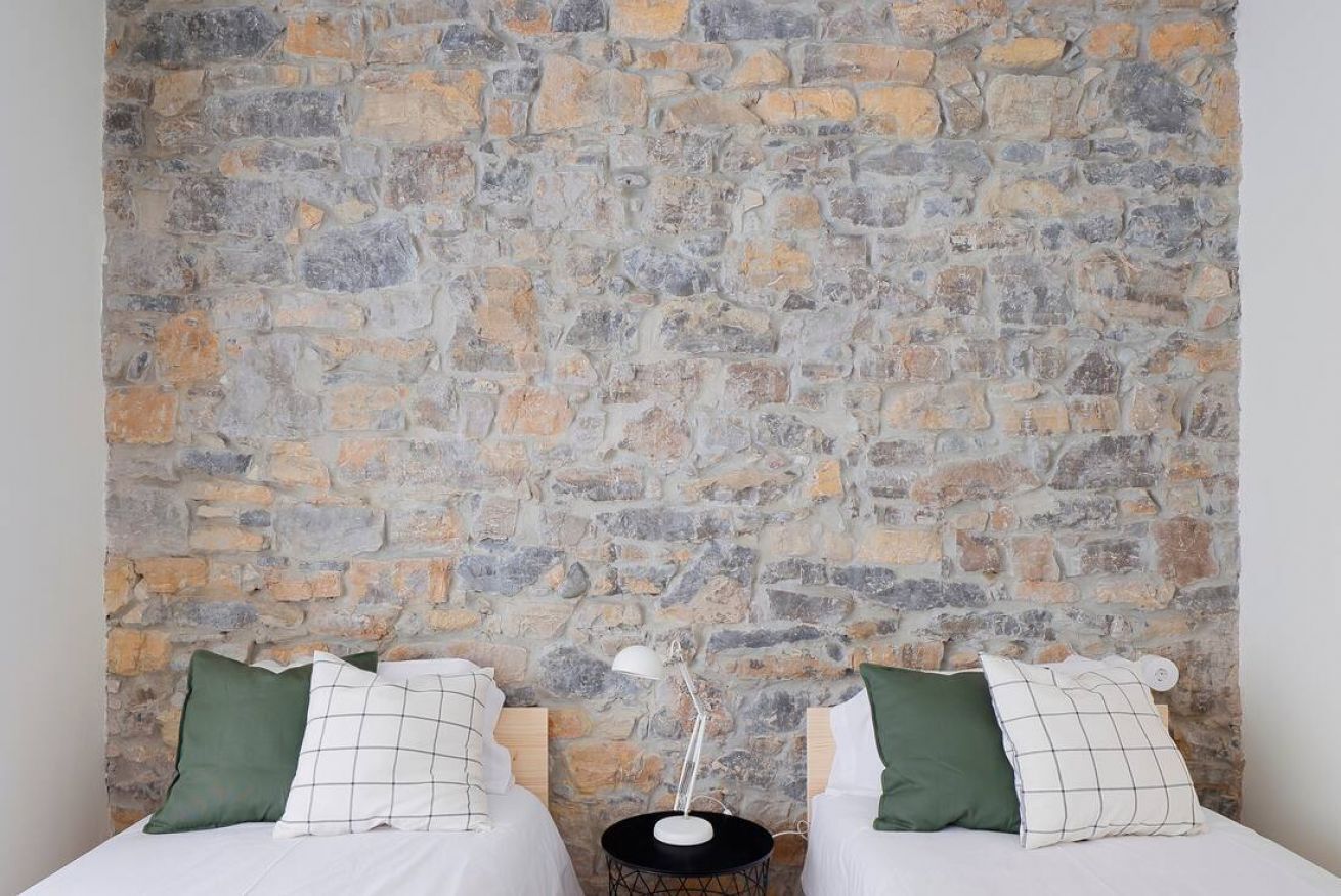 Une chambre avec deux lits adossés à un mur en pierre, chaque lit étant muni d’un oreiller et d’une lampe de chevet.