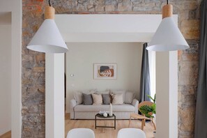 A living room with a stone wall, a sofa, two white chairs, a small table with a vase, and two pendant lights.