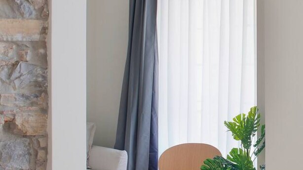 Ein Zimmer mit Steinwand, einem weißen Stuhl, einem runden Holztisch und einer Pflanze.