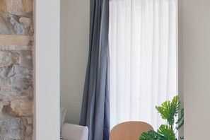 Ein Zimmer mit Steinwand, einem weißen Stuhl, einem runden Holztisch und einer Pflanze.