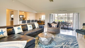 A spacious living area with a black leather sofa, a round coffee table, and a patterned rug. A sign reading "Cape Coral, Florida" is visible in the background.
