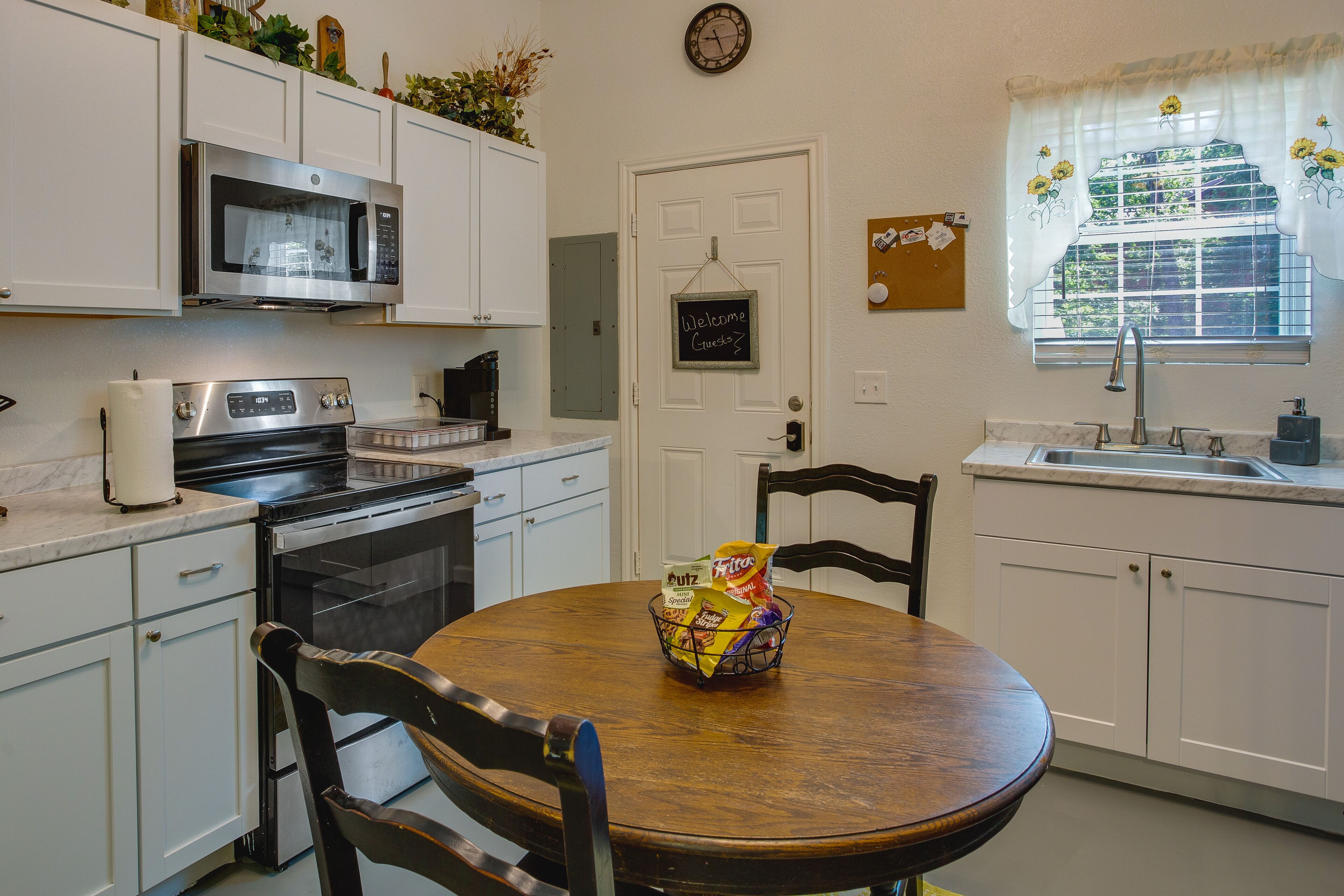 A kitchen with white cabinets, a microwave, an oven, a sink, and a wooden dining table with chairs.