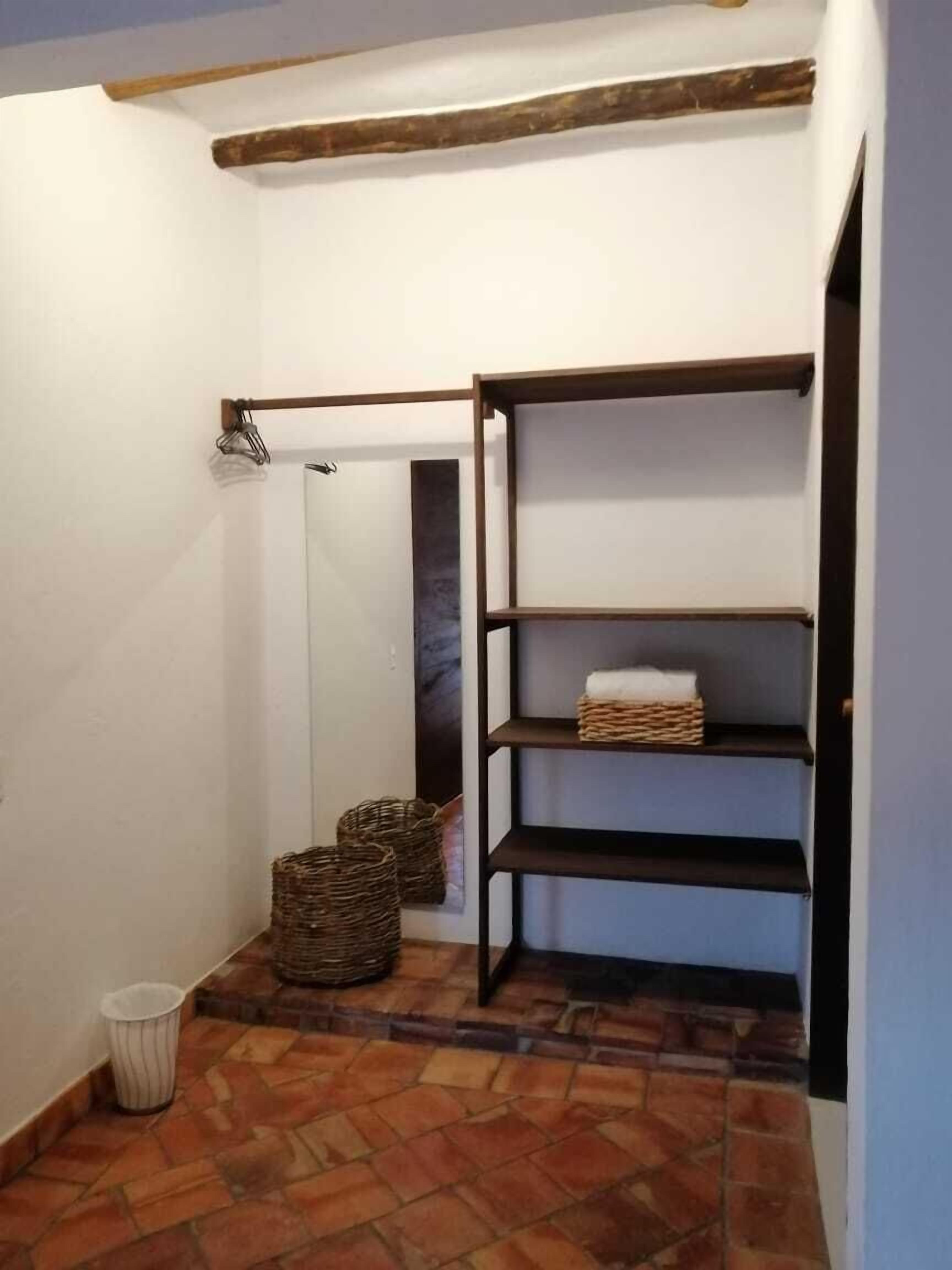 A corner with a tiled floor, a wooden beam ceiling, a white wall, and a black metal shelf unit with baskets.
