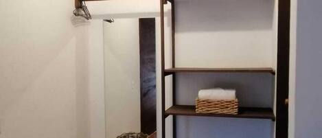 A corner with a tiled floor, a wooden beam ceiling, a white wall, and a black metal shelf unit with baskets.