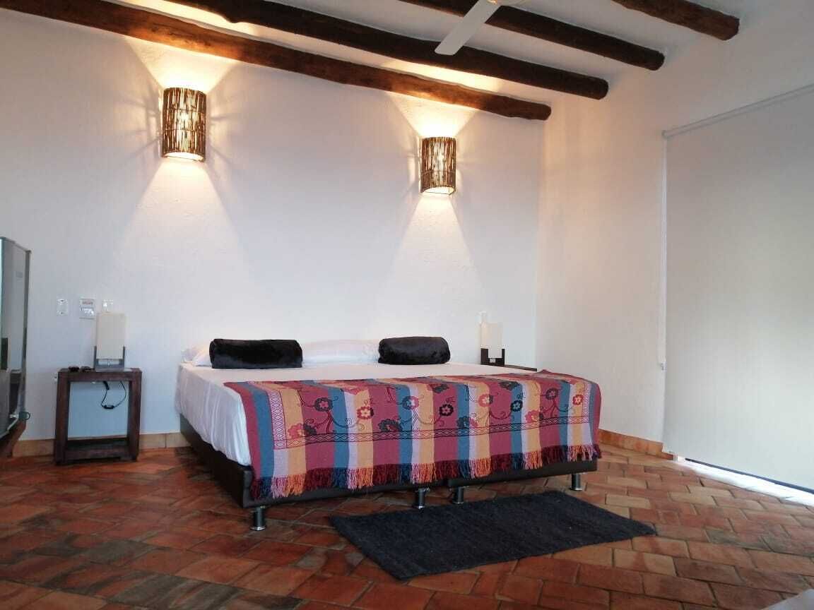 Un dormitorio con una cama, dos lámparas de pared, una mesita de noche y suelo de ladrillo.
