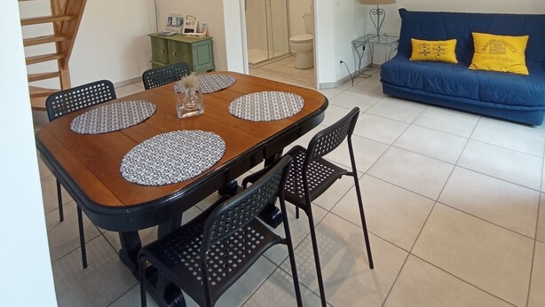 A dining area with a wooden table and black chairs, a blue sofa with yellow pillows, and a staircase. - Le Penty Gîte (Plestin-les-Grèves)