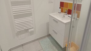 A bathroom with a white sink, a mirror, a towel rack, and a shower area. - Le Penty Gîte (Plestin-les-Grèves)
