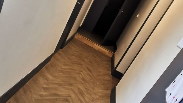 A hallway with a wooden floor, a black door, and a ceiling light. - Nuit Tendance à Mâcon 1 (Mâcon)