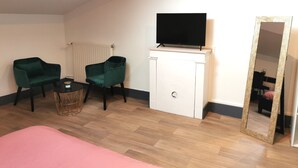 A room with a bed, two green armchairs, a small table with a basket, a white cabinet with a TV, and a large mirror. - Nuit Tendance à Mâcon 1 (Mâcon)