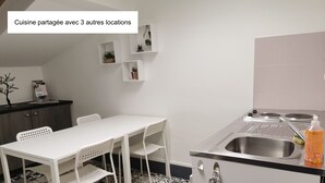 A compact kitchen with a white table and chairs, a built-in stove, and a sink. There are three small shelves above the stove. - Nuit Tendance à Mâcon 1 (Mâcon)