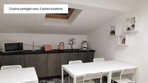 A modern kitchen with a microwave, toaster, and kettle on the counter, a white dining table with chairs, and patterned floor tiles. - Nuit Tendance à Mâcon 1 (Mâcon)