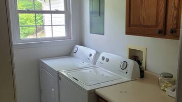 A compact laundry room with a washer and dryer, a window with a view of greenery, and wooden cabinets.