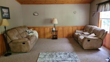 A cozy living room with a wooden ceiling, two sofas, a small table with a lamp, and a rug.
