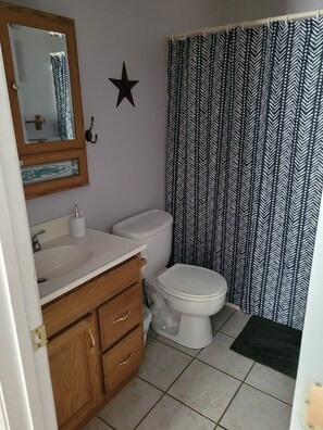 Une salle de bain avec un meuble-lavabo en bois, un lavabo blanc, des toilettes et une décoration en forme d’étoile noire sur le mur.