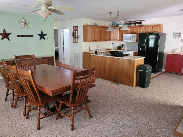 A kitchen with wooden cabinets, a black refrigerator, a microwave, and a dining area with a wooden table and chairs.