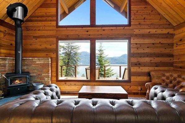 L’intérieur chaleureux d’un chalet avec une cheminée, un canapé en cuir et une grande fenêtre donnant sur un paysage montagneux magnifique.