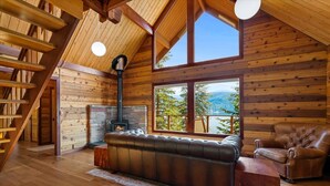 Ein gemütliches Blockhaus-Interieur mit Kamin, Ledersofa und einem großen Fenster mit Panoramablick.