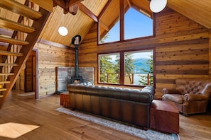 L’intérieur chaleureux d’un chalet en bois, avec une cheminée, un canapé en cuir et une grande fenêtre offrant une vue panoramique.