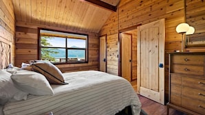Ein Schlafzimmer in einer Holzhütte mit Bett, Kommode und einem Fenster mit Blick.