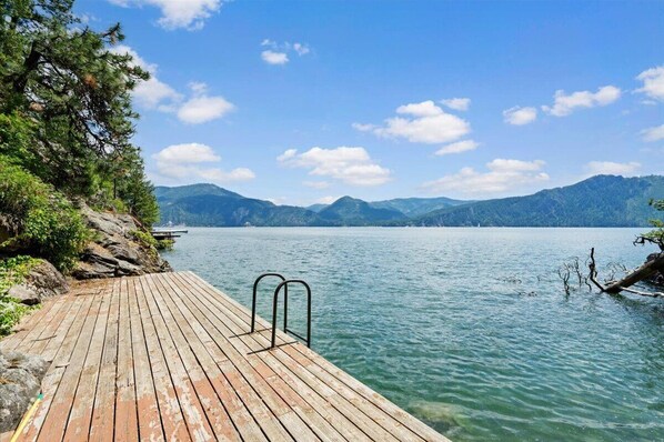 Guests can enjoy a serene lake view from this dock surrounded by lush greenery and distant mountains.