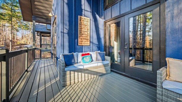 A wooden deck with a sofa and cushions, a sign with porch rules, and a large window.